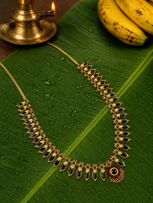 Classic emerald black stone variant of the South Indian Nagapadam gold necklace arranged neatly on a light green banana leaf background.