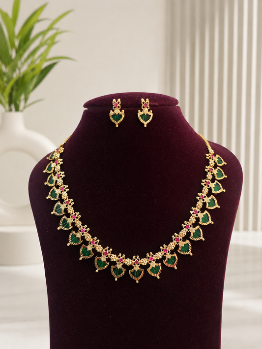 A ruby red leaf-shaped Kerala style Palakka necklace set with matching earrings, arranged on a banana leaf background with a yellow banana and decorative parchment paper.
