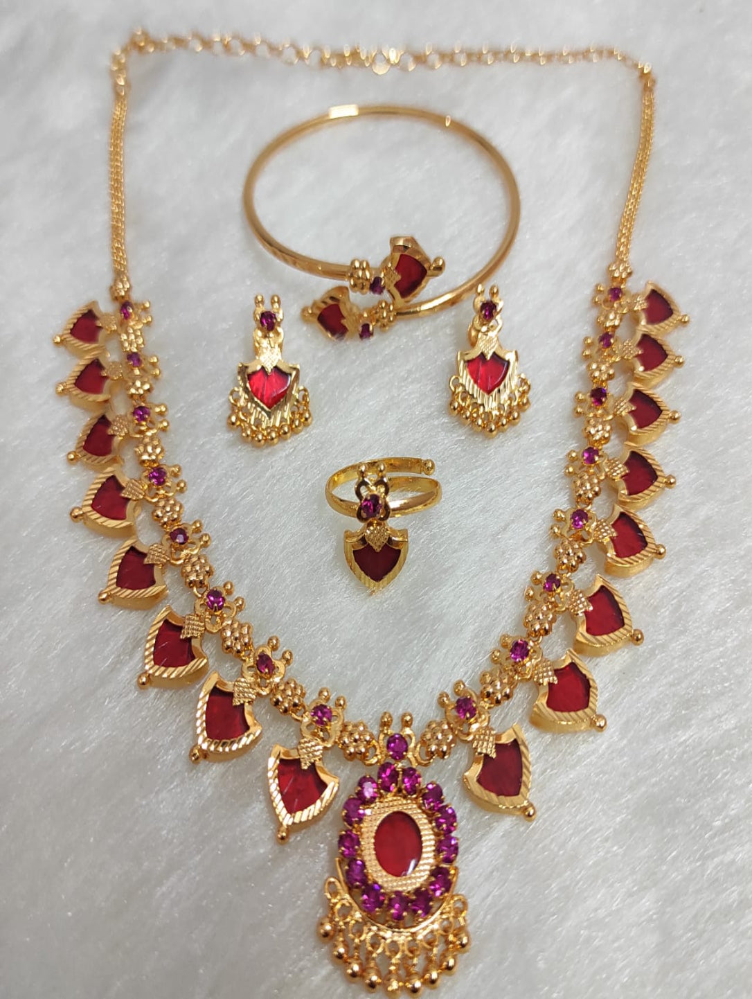 Gold jewelry set with red stones on a light gray background