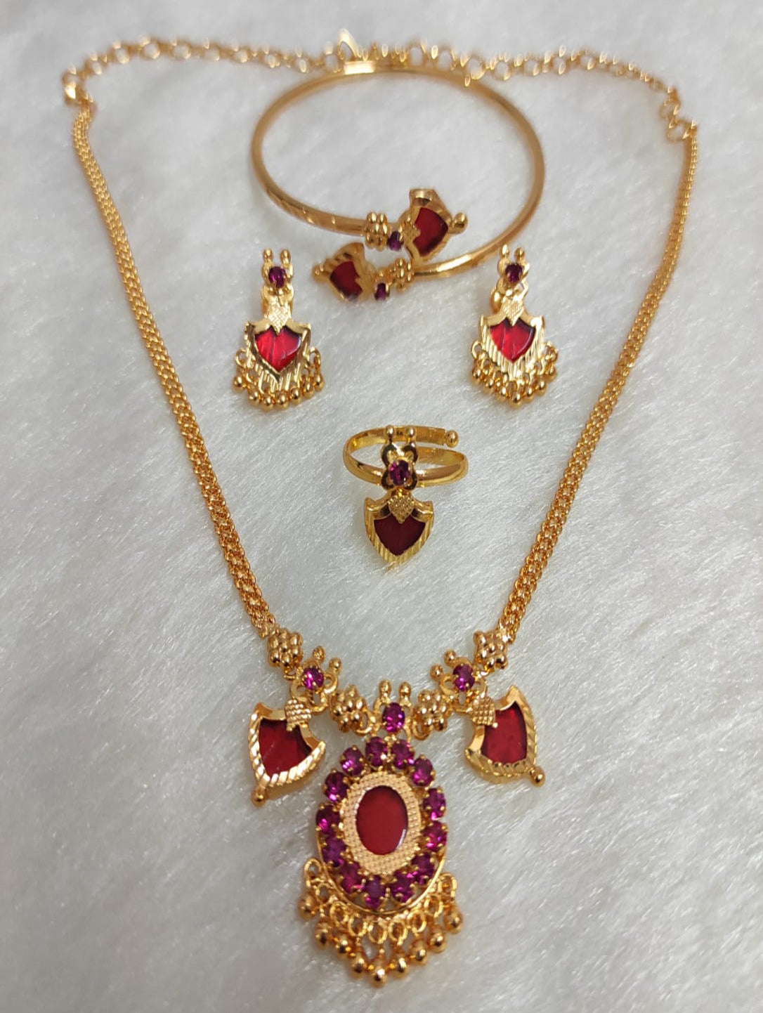 Triveni 2 Charm gold-plated jewelry combo set featuring a traditional necklace, earrings, ring, and bangle with ruby red stones on a white background.