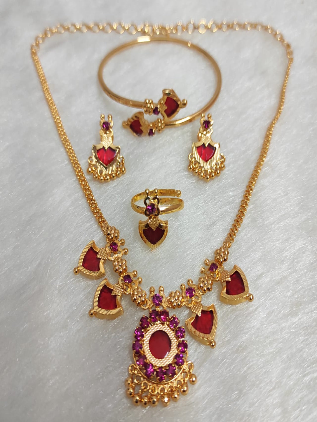 Gold jewelry set with red stones on a light gray background