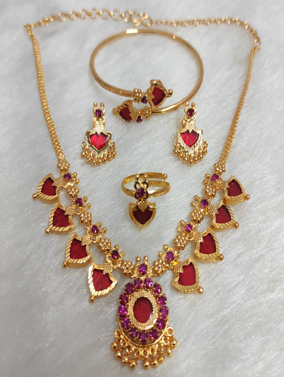 Gold jewelry set with red heart-shaped stones on a white background