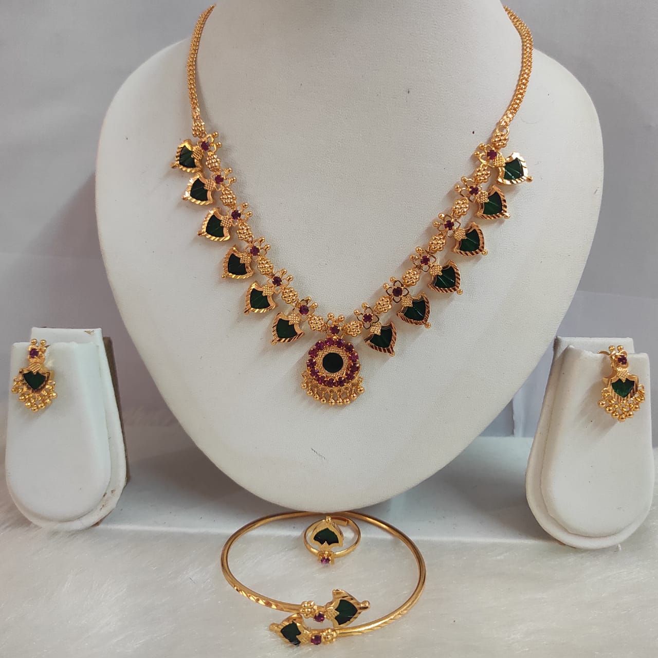 Gold necklace with green and red stones on a white stand, accompanied by matching earrings.