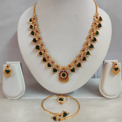 Gold necklace with green and red gemstones on a white mannequin bust, accompanied by matching earrings and a bracelet.