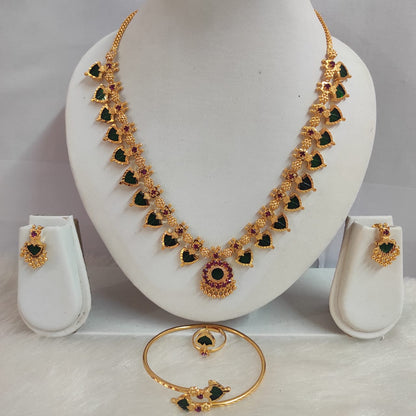 Gold necklace with green and red stones on a white stand, accompanied by earrings and a bracelet.