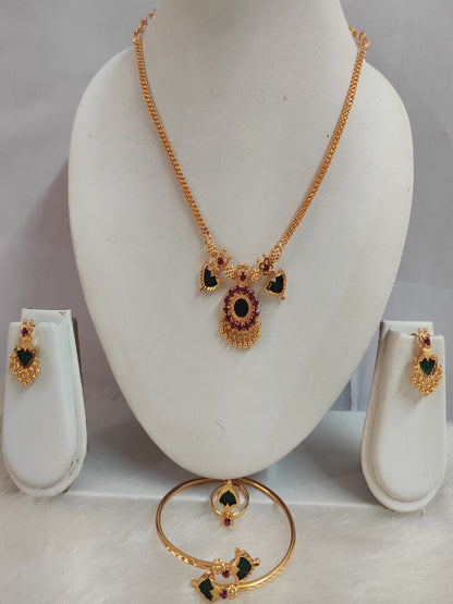 Naidila 2 Charm gold-plated jewelry combo set displaying a traditional necklace, earrings, kada, and a ring with emerald green and ruby red stones on jewelry mannequins.