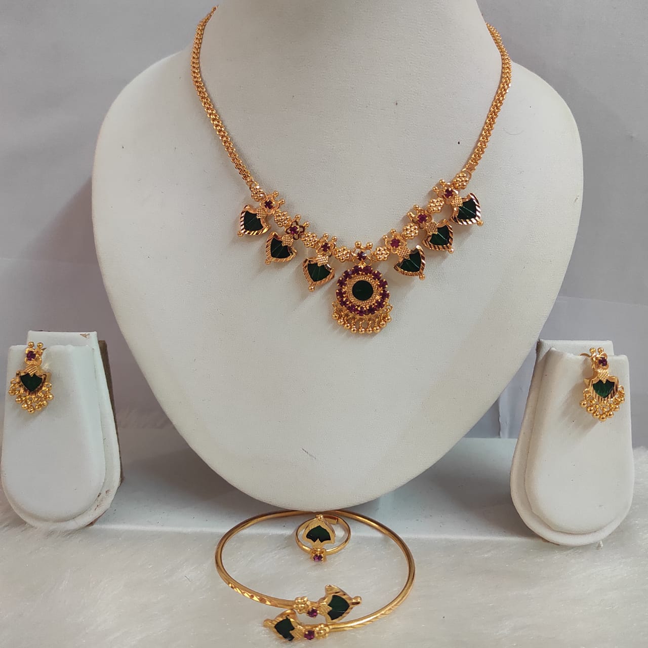 Gold necklace with green gemstones on a mannequin bust, accompanied by matching earrings and a bracelet.