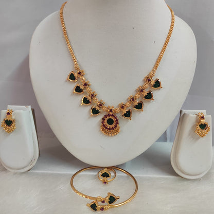 Gold necklace with green and red gemstones on a white stand, accompanied by matching earrings and bangles.