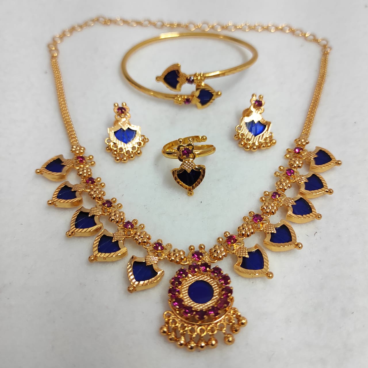 Gold jewelry set with blue and red stones on a light gray background