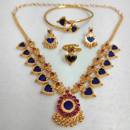 Nandika 12 Charm gold-plated jewelry set featuring a traditional necklace, matching earrings, a ring, and a bangle with deep sapphire blue and ruby stones on a white surface.