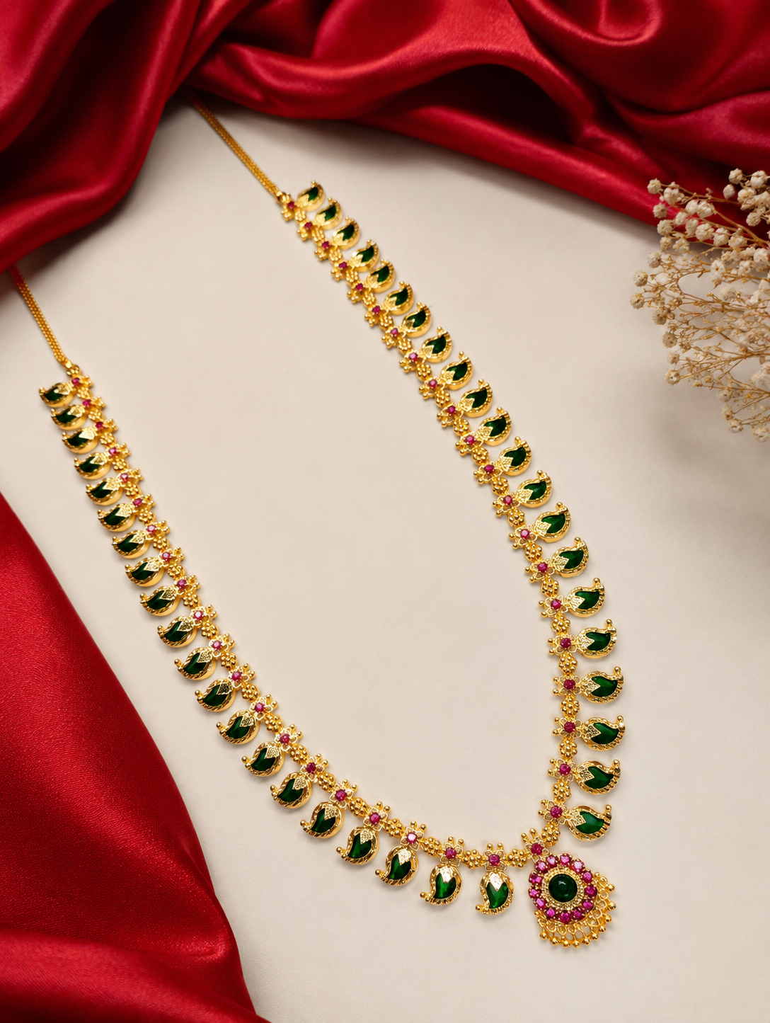 Gold necklace with green and red stones on a red fabric background