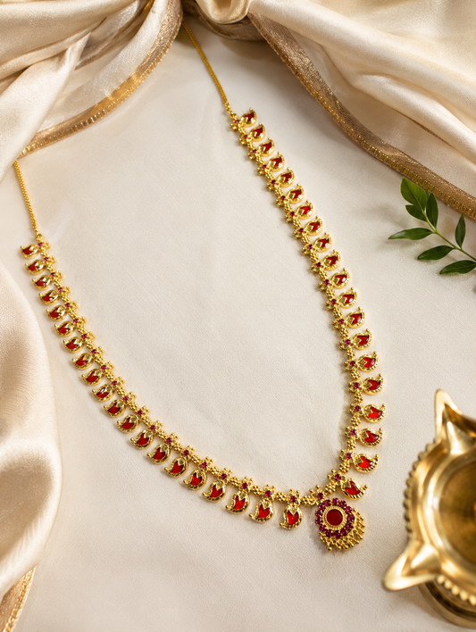 Gold necklace with red stones on a white surface with a gold Diya lamp.