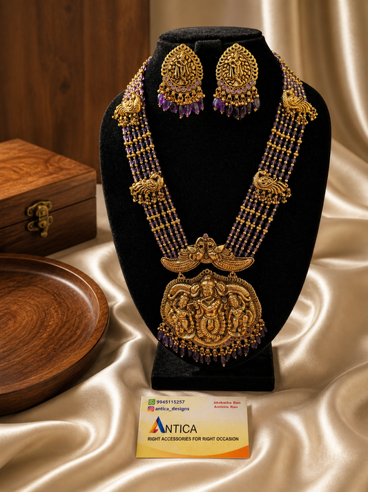 Gold necklace and earrings on a black stand with a Antica label, on a beige fabric background.
