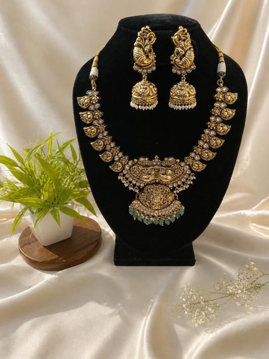 Gold necklace and earrings set on a black stand with a white fabric background