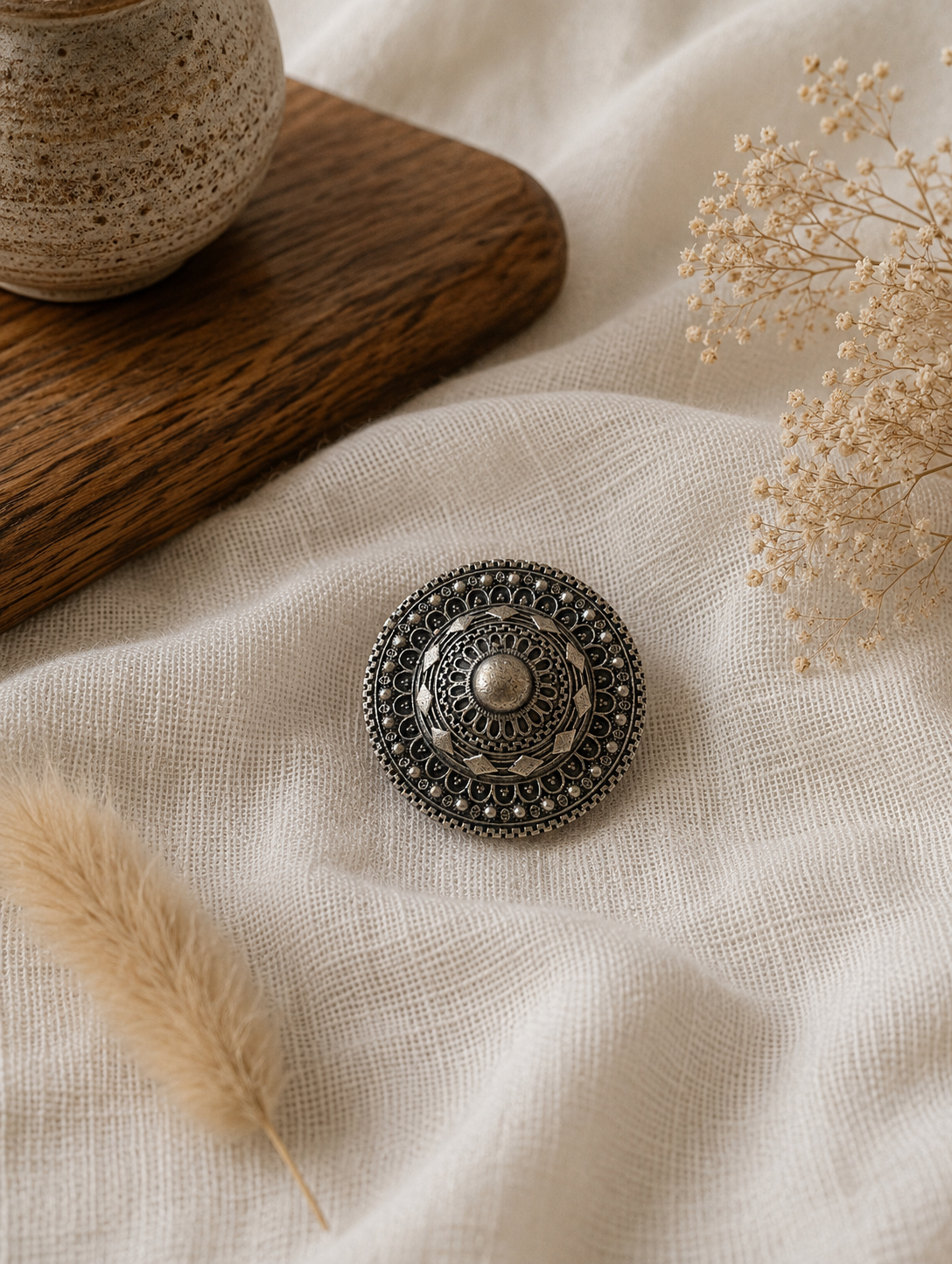 Decorative silver hair pin on a textured fabric surface with dried plants
