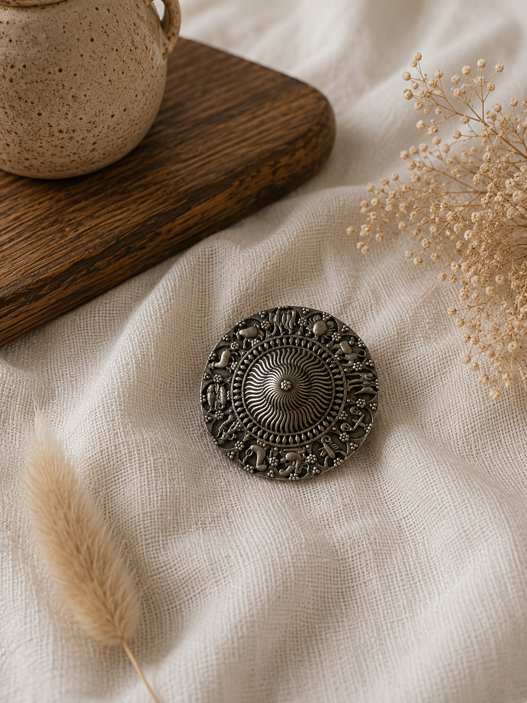 Decorative metal hair pin on a textured fabric surface with dried plants and a wooden board.
