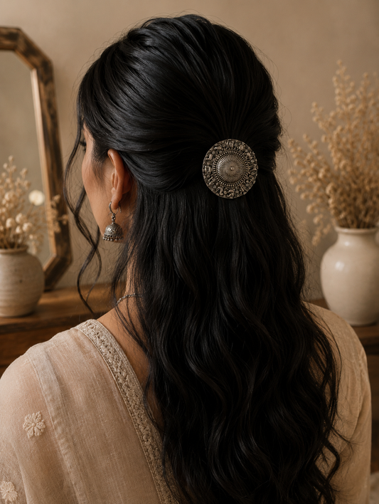 A back view of a woman with long, dark wavy hair styled in a graceful half-updo, secured with a minimalist hexagon-shaped silver hair pin. The accessory features a geometric hollow hexagonal outline detailed with delicate traditional metal beadwork along its edges.