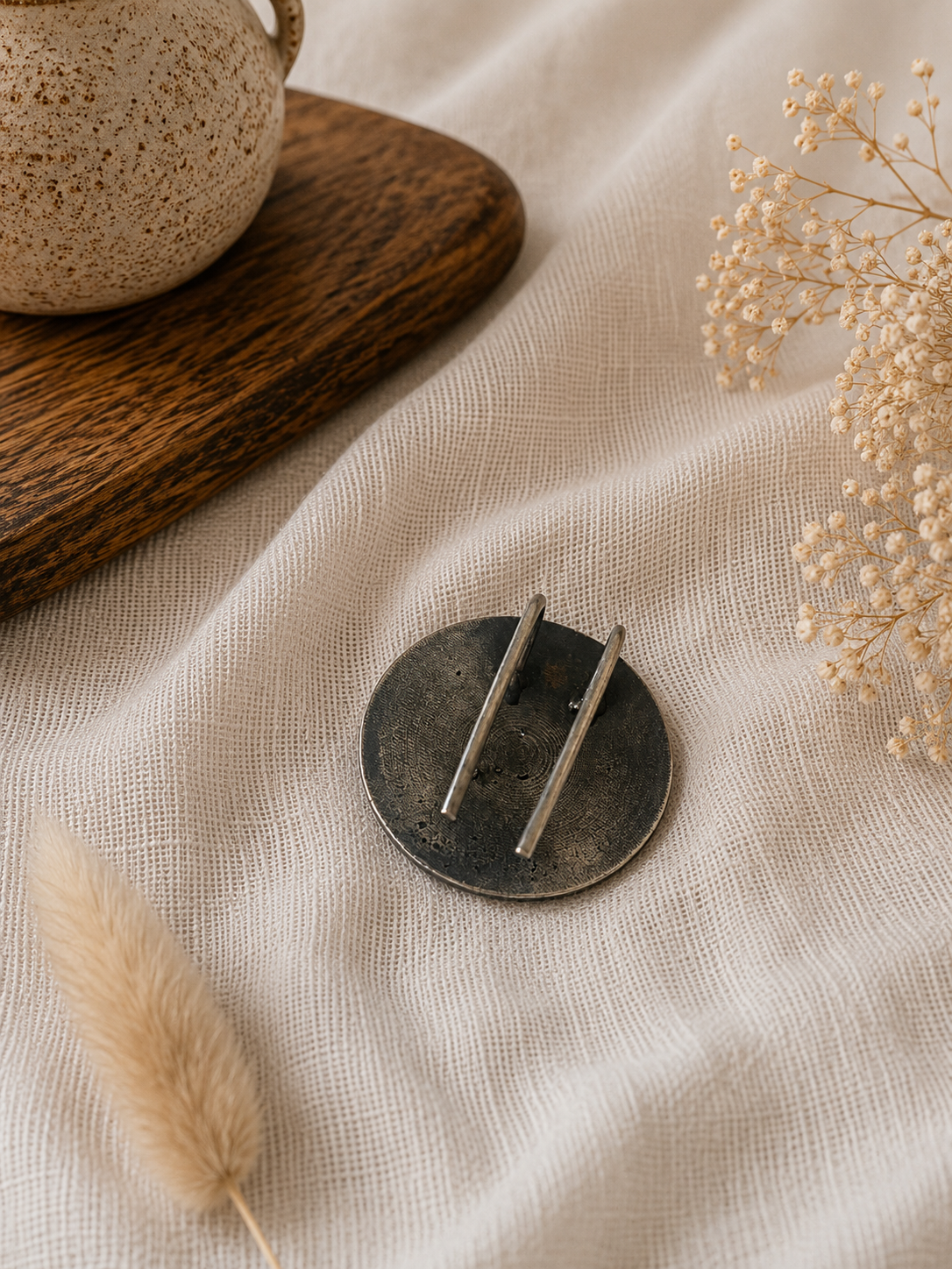 Round metallic object with two sticks on a textured beige surface with dried plants.
