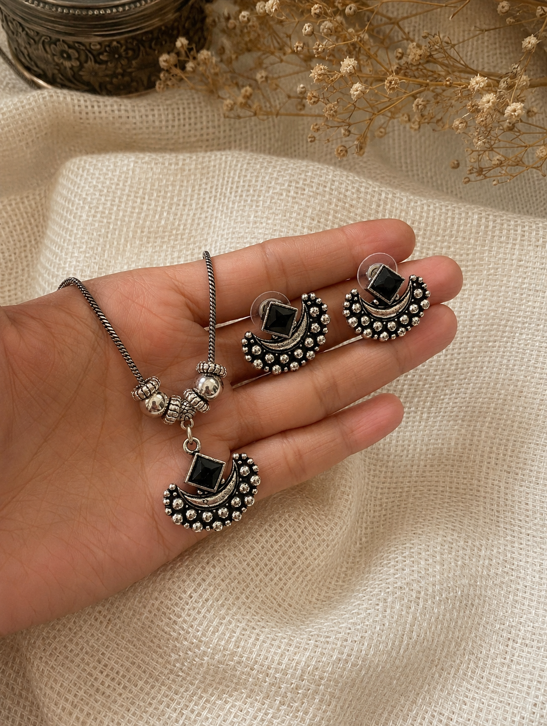 Hand holding silver jewelry set with black stones on a textured beige surface