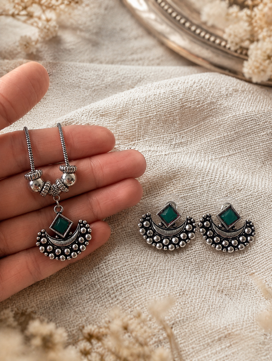 Silver earrings with green gemstones held by a hand on a textured surface.