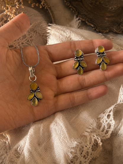 Hand holding silver and yellow leaf-shaped jewelry on a textured fabric background