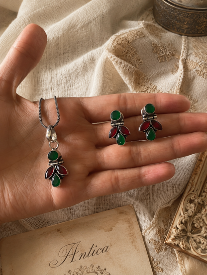 Hand holding a pair of green and red jewelry set on a textured fabric background