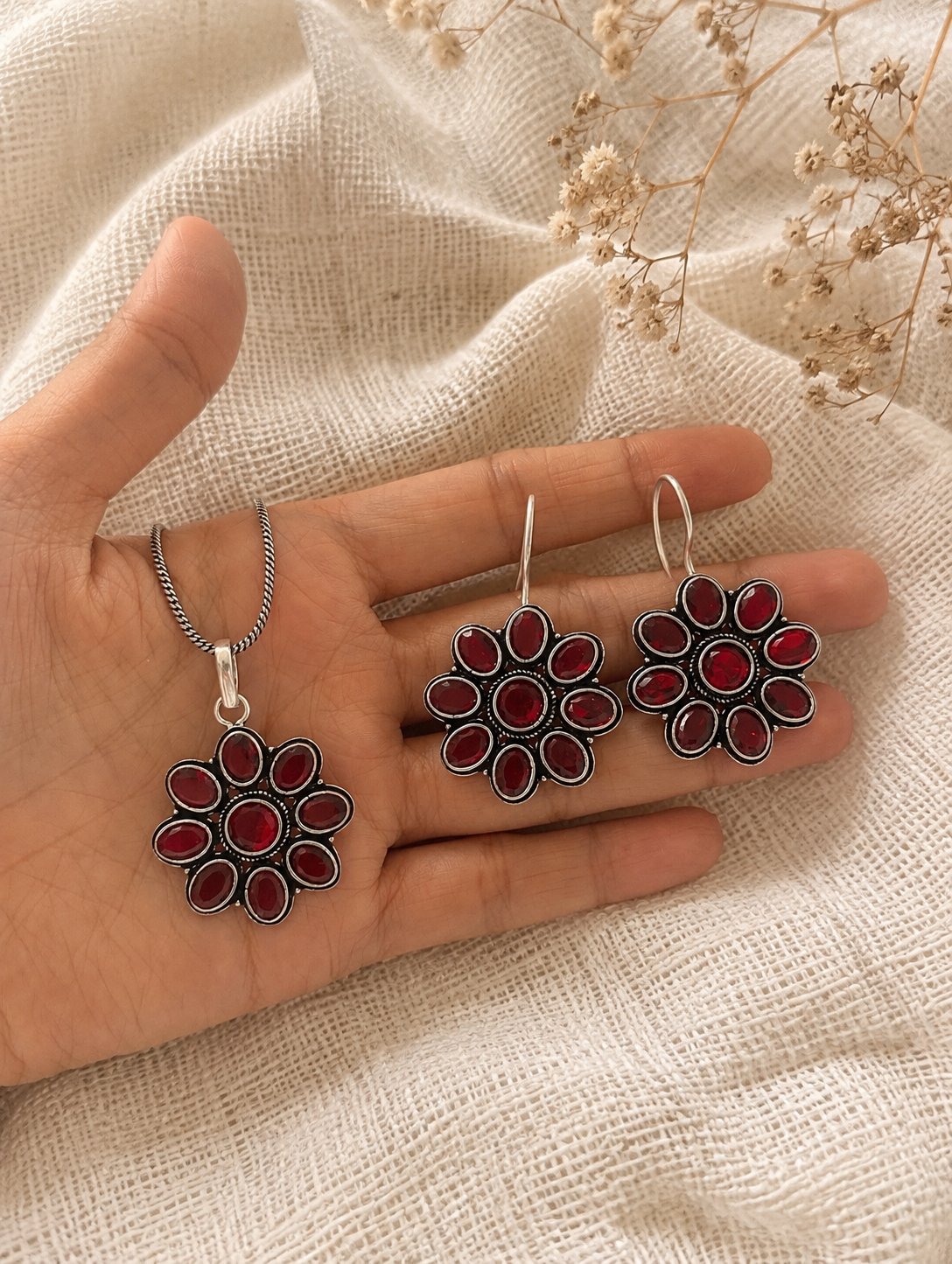 Hand holding silver earrings with red stones on a textured fabric background