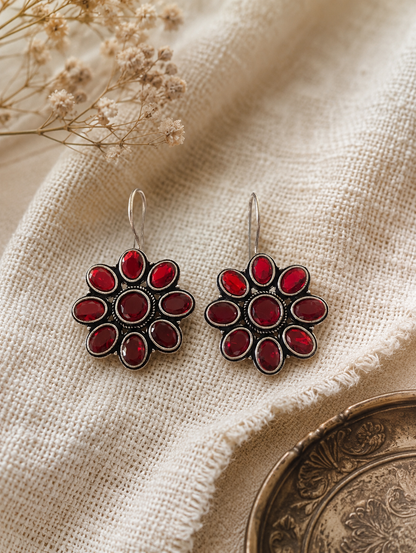 Pair of red floral earrings on a textured beige fabric background