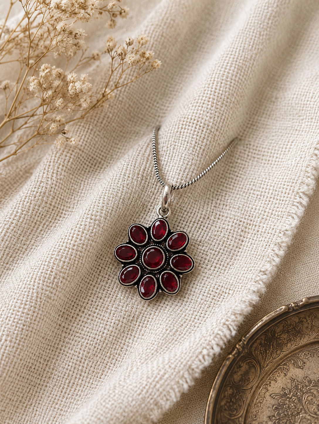 Silver necklace with a red pendant on a textured beige fabric background