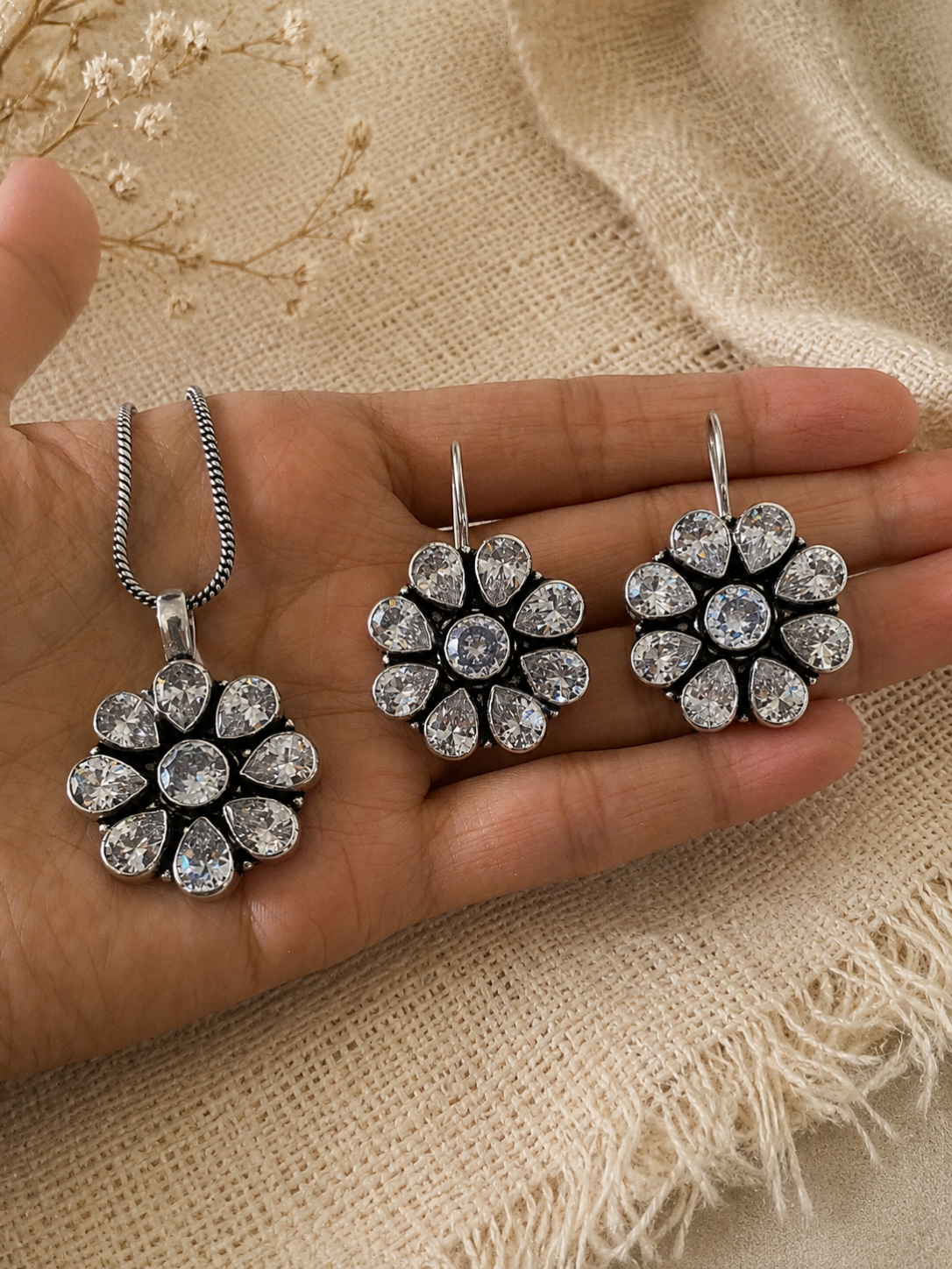 Silver floral jewelry set on a hand with a beige fabric background