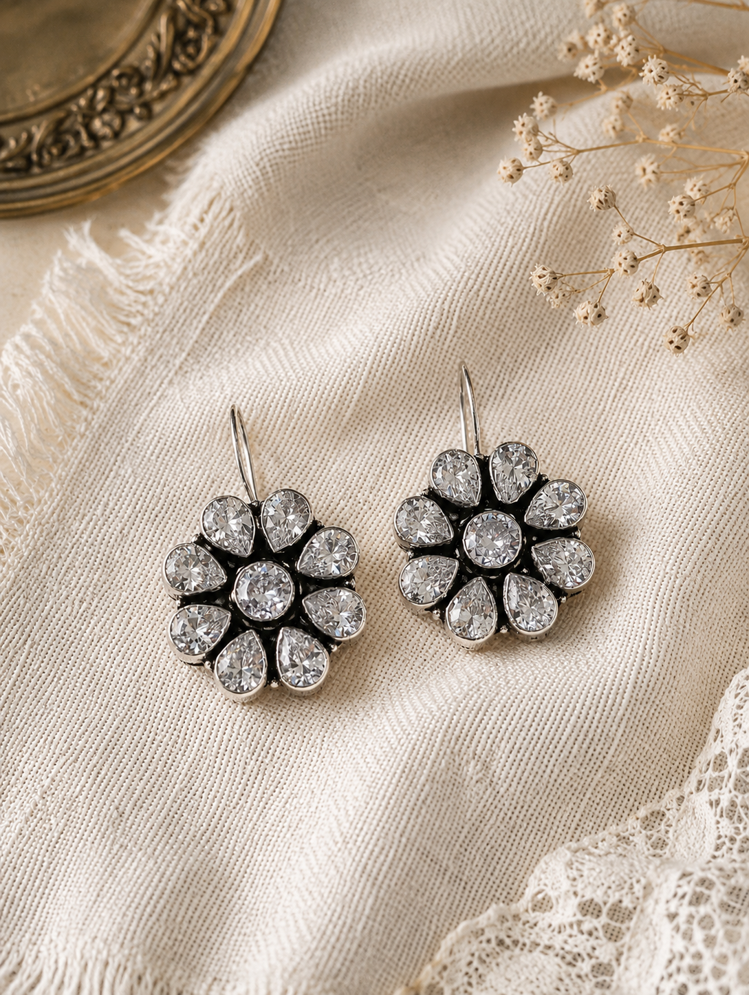 Pair of silver floral earrings on a textured fabric background