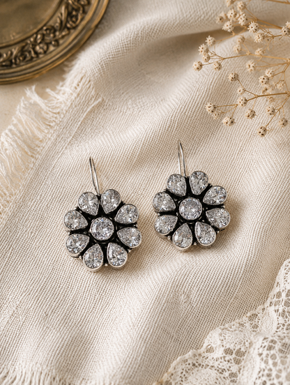 Pair of silver floral earrings on a textured fabric background