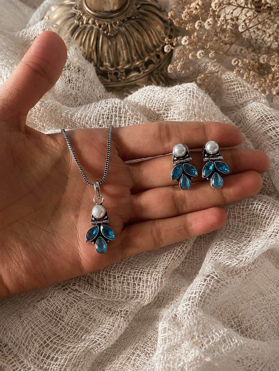 Hand holding a necklace and earrings with blue and white gemstones on a textured fabric background