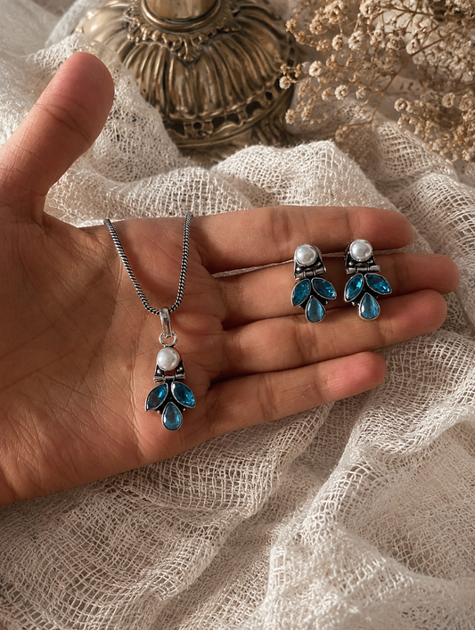 Hand holding a necklace and earrings with blue and white gemstones on a textured fabric background