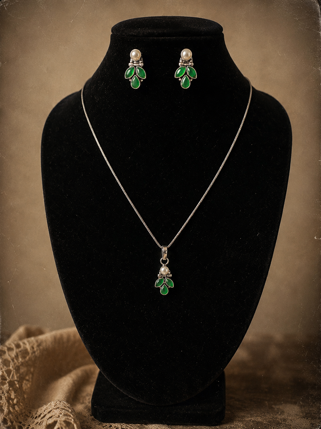 Jewelry set with necklace and earrings on a black velvet stand against a brown background