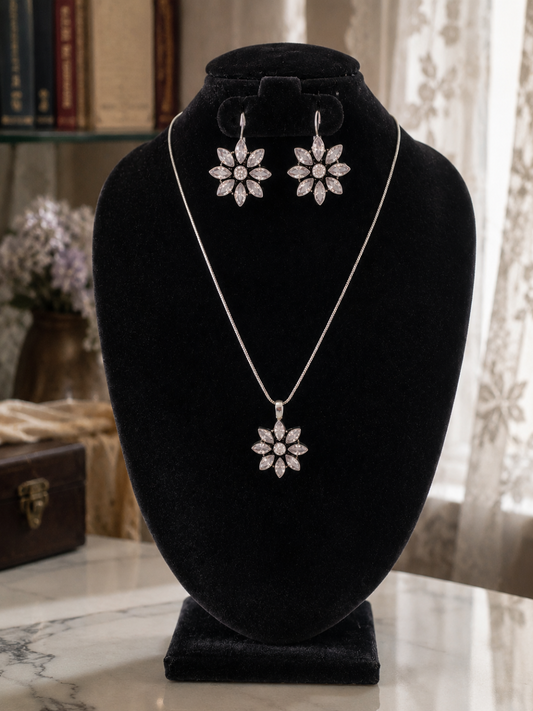 A matching oxidized silver jewelry set displayed on a black velvet bust stand, featuring a fine chain necklace with a starburst-shaped clear crystal pendant and matching multi-petal crystal dangle hook earrings.