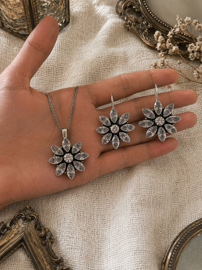 Hand holding silver floral jewelry set with decorative frames and flowers in the background
