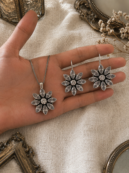 Hand holding silver floral jewelry set with decorative frames and flowers in the background