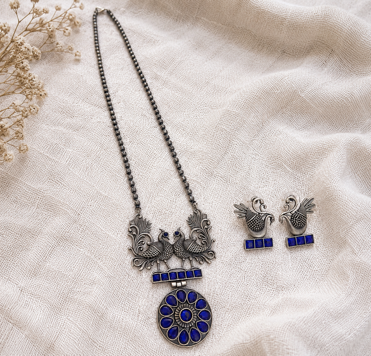Silver necklace with blue accents and matching earrings on a beige fabric background