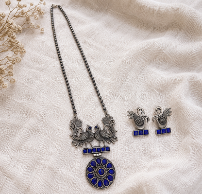 Silver necklace with blue accents and matching earrings on a beige fabric background