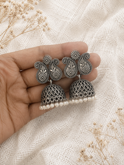 Silver earrings with intricate designs held between fingers on a textured beige background.