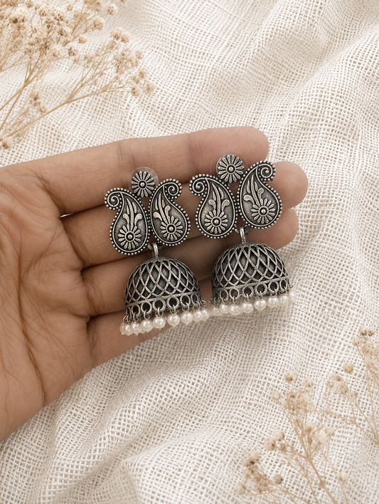Silver earrings with intricate designs held between fingers on a textured beige background.