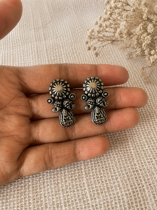 Silver earrings held between fingers on a textured fabric background