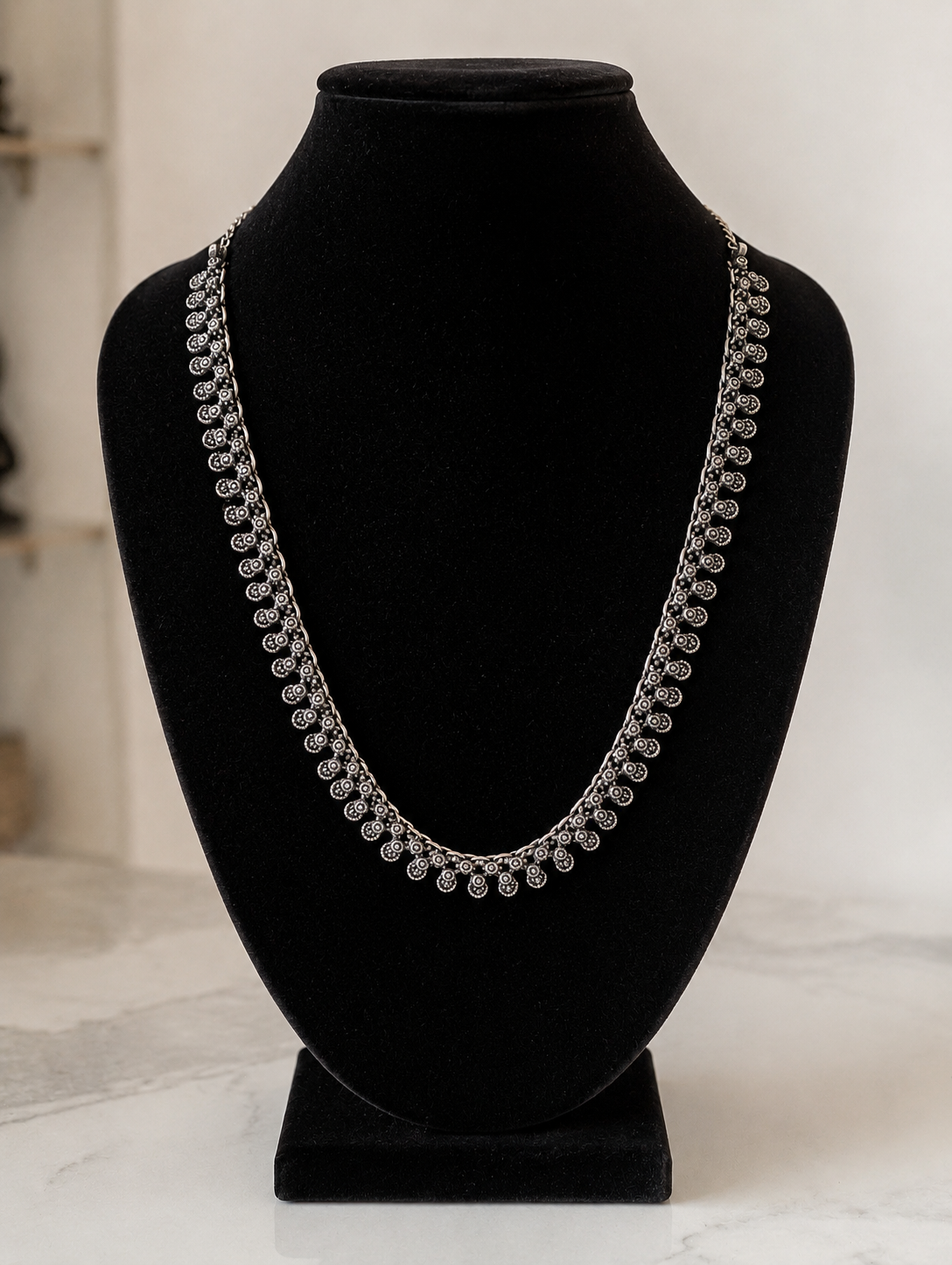 Silver necklace on a black mannequin bust against a white background