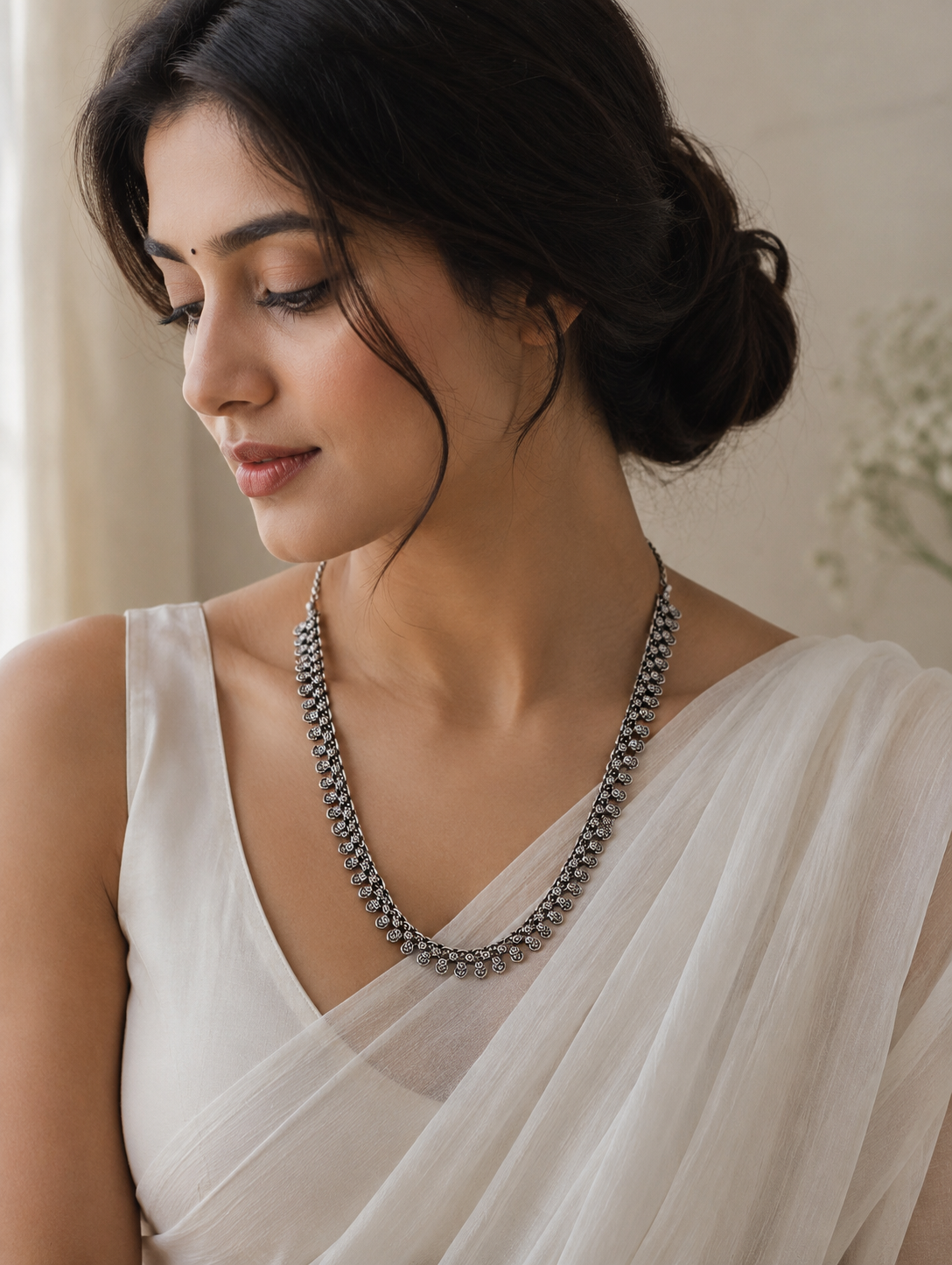 Woman wearing a white saree with a silver necklace against a neutral background