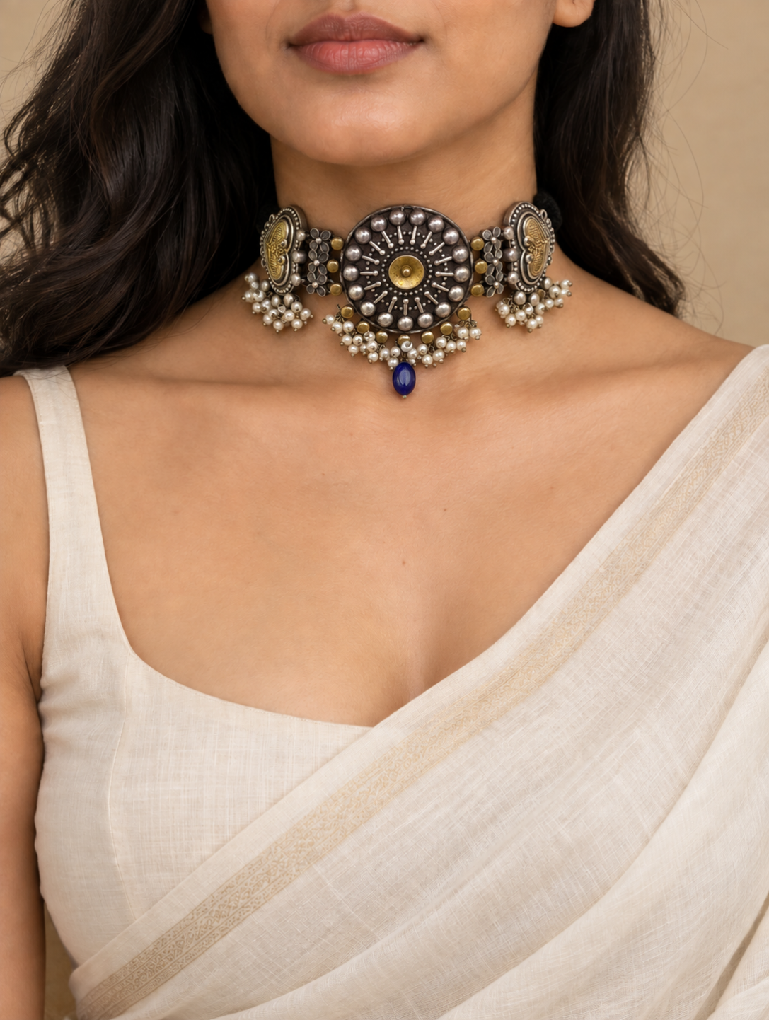 Woman wearing an antique dual-tone oxidized choker necklace featuring a circular sunburst medallion, pearl cluster dangles, and a central blue stone drop.