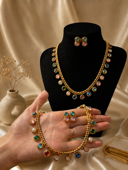 A delicate and elegant jewelry set held in a hand over a rich brown satin fabric background. The set includes a slender gold-plated necklace decorated with closely spaced, teardrop-shaped white pearls, paired with matching compact pearl drop earrings.