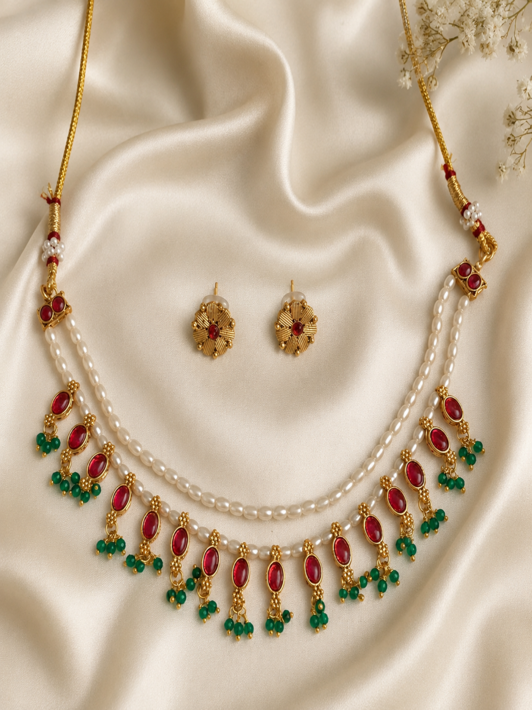 Gold necklace with red and green stones on a beige fabric background