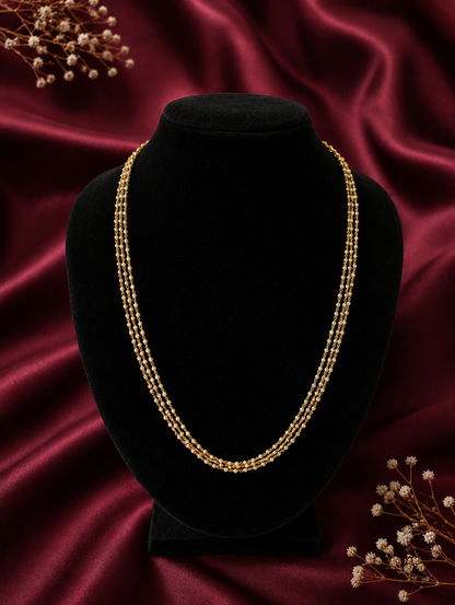 A dainty three-layered gold chain necklace featuring tiny woven seed pearls, displayed beautifully on a black velvet bust mannequin against a maroon satin background.