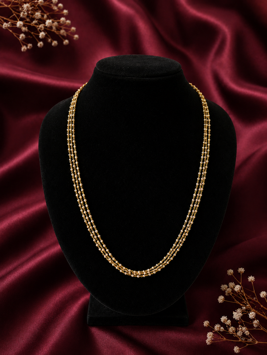 A dainty three-layered gold chain necklace featuring tiny woven seed pearls, displayed beautifully on a black velvet bust mannequin against a maroon satin background.